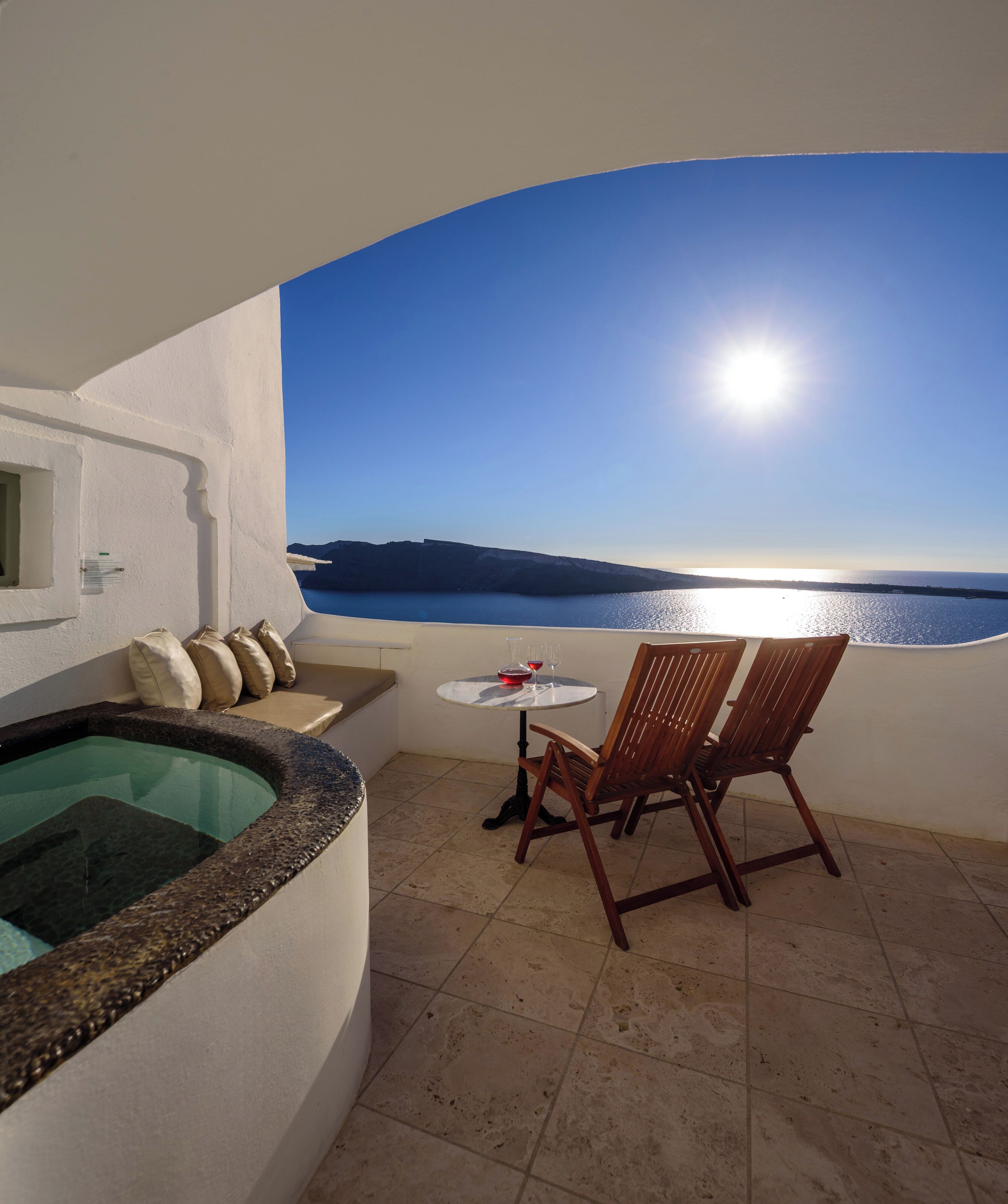 Ein Balkon mit Whirlpool, einem Tisch und zwei Stühlen, mit Blick auf das Meer und die Berge.