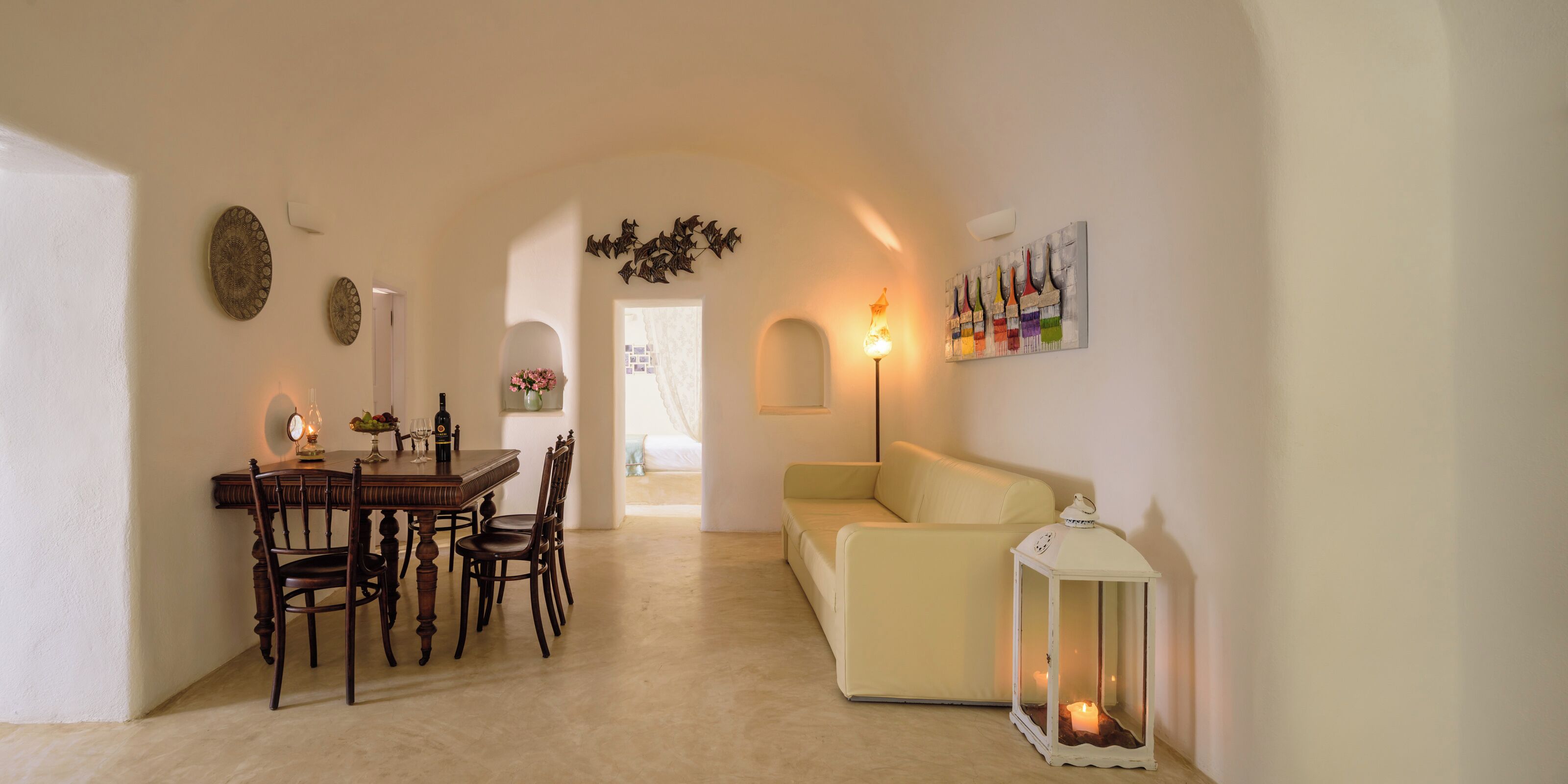 Un comedor con una mesa y sillas de madera, un sofá y una mesita con un florero y velas.
