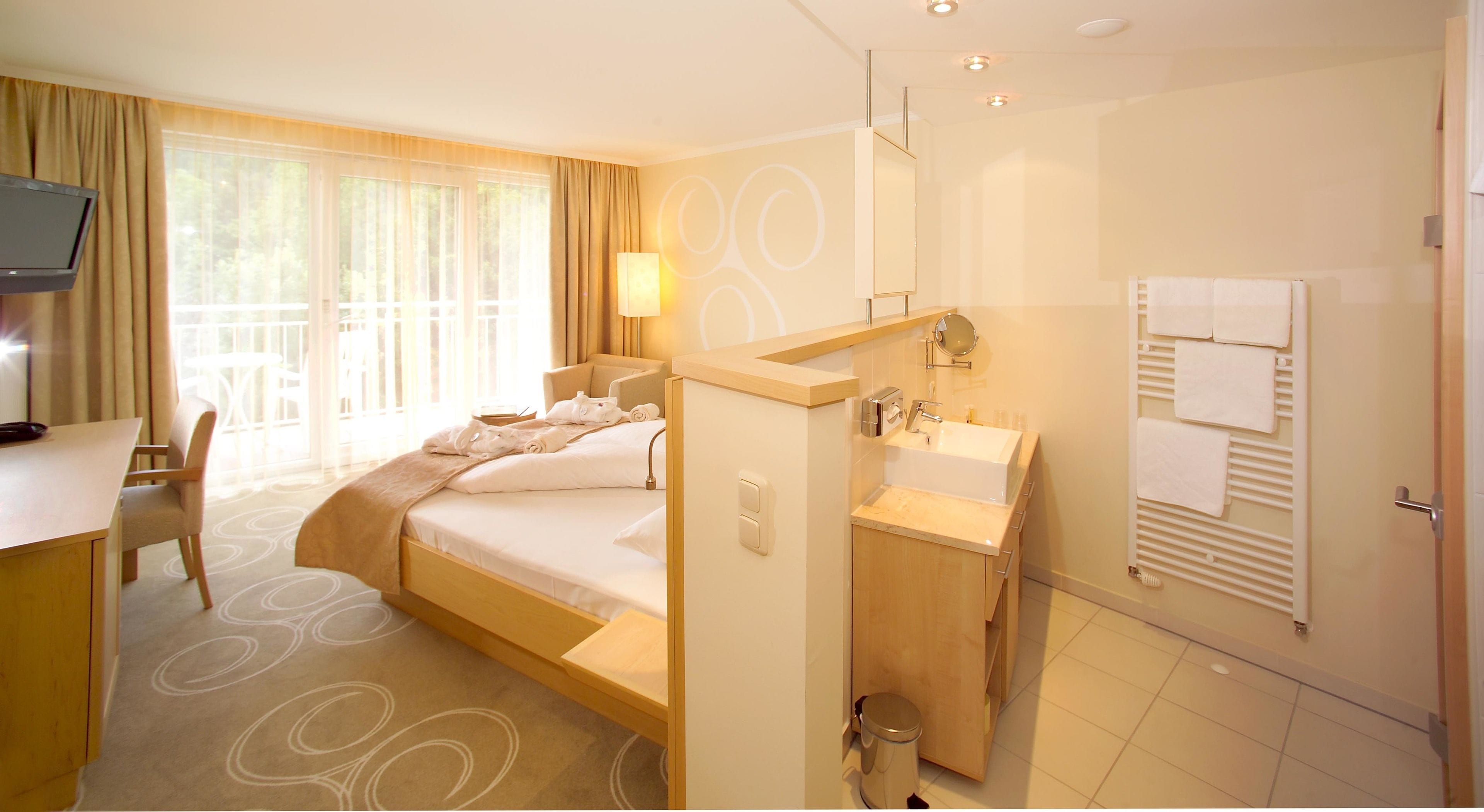 Habitación de hotel con cama, escritorio, baño con lavamanos y espejo, y televisor sobre el escritorio.