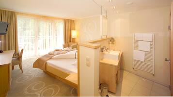 Habitación de hotel con cama, escritorio, baño con lavamanos y espejo, y televisor sobre el escritorio.