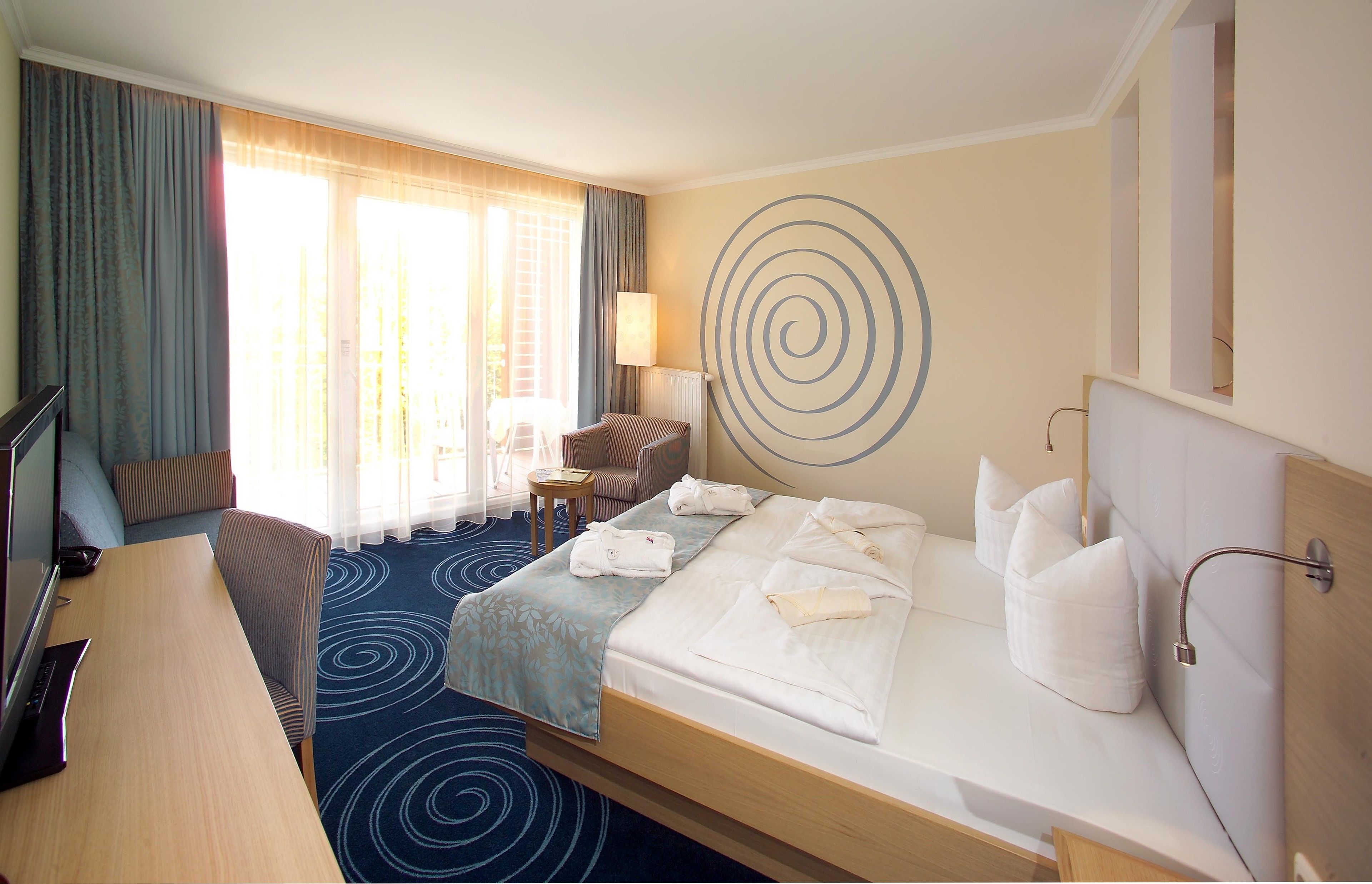 A hotel room with a bed, a desk, a chair, a TV, and a view of the outdoors.