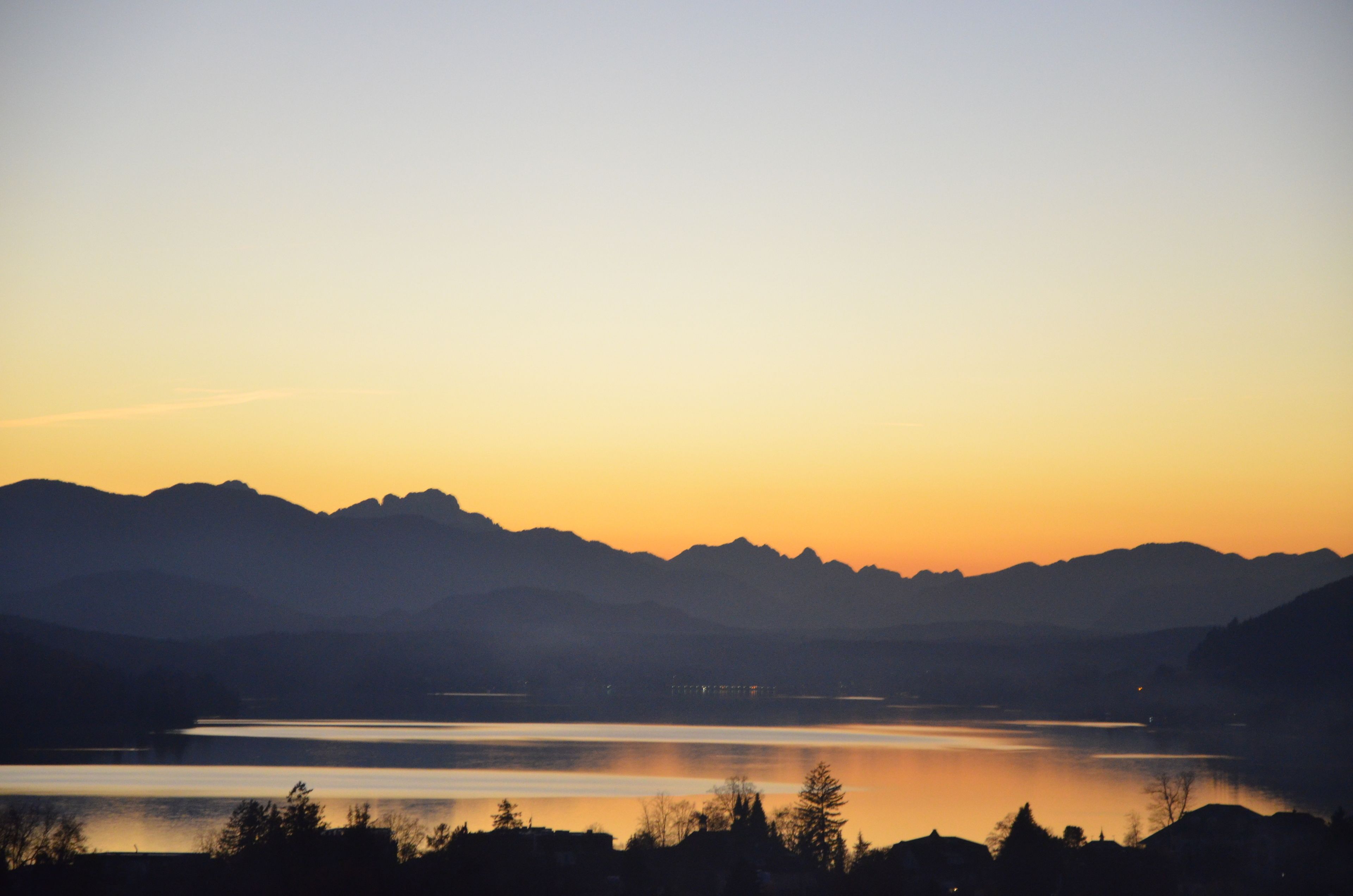 Una vista panorámica de un lago al atardecer con montañas al fondo.