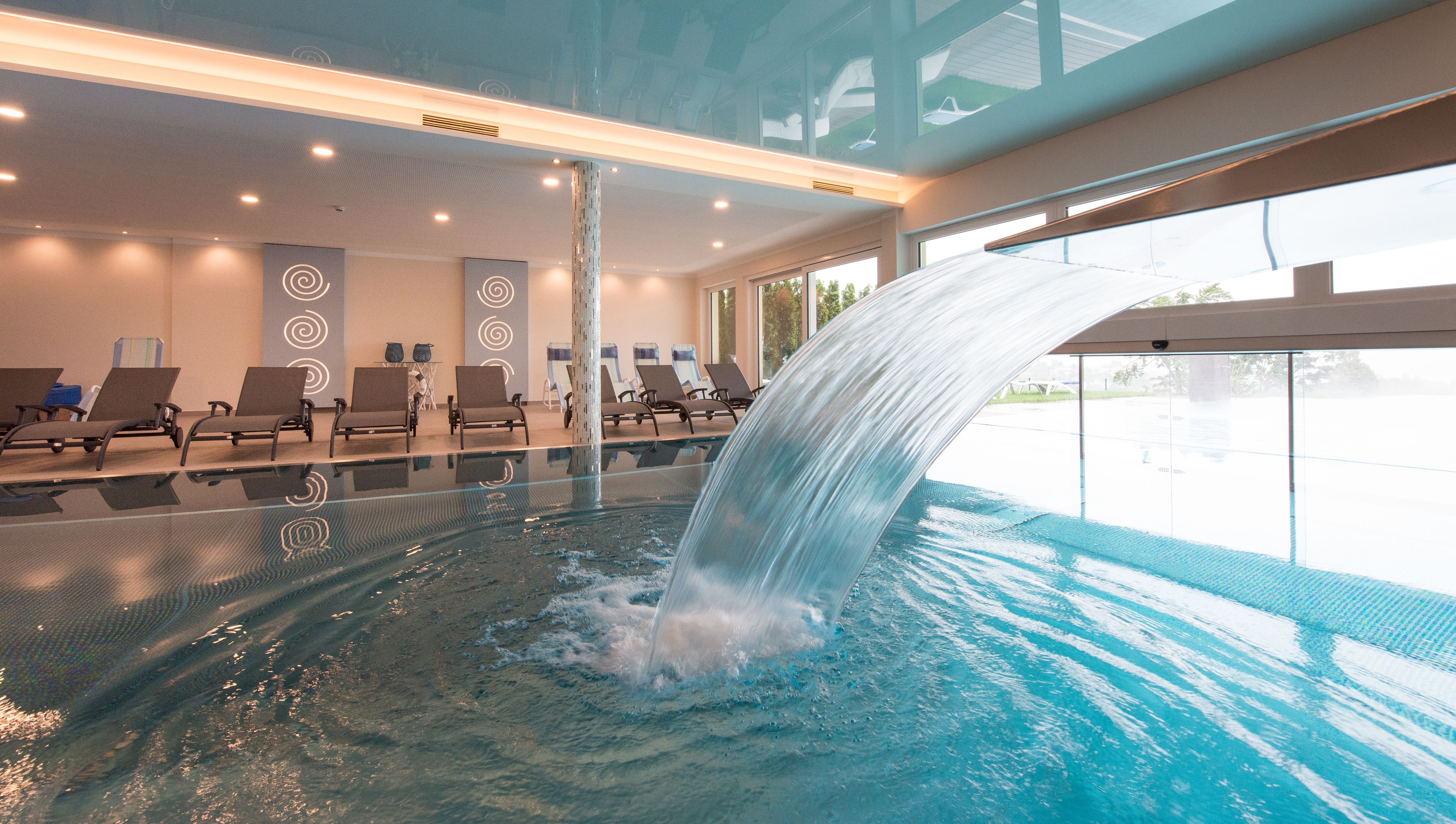 Una piscina con cascada, sillas de descanso y vistas al exterior.