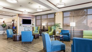A hotel lobby with blue and green chairs, a flat-screen TV, a fireplace, and large windows.