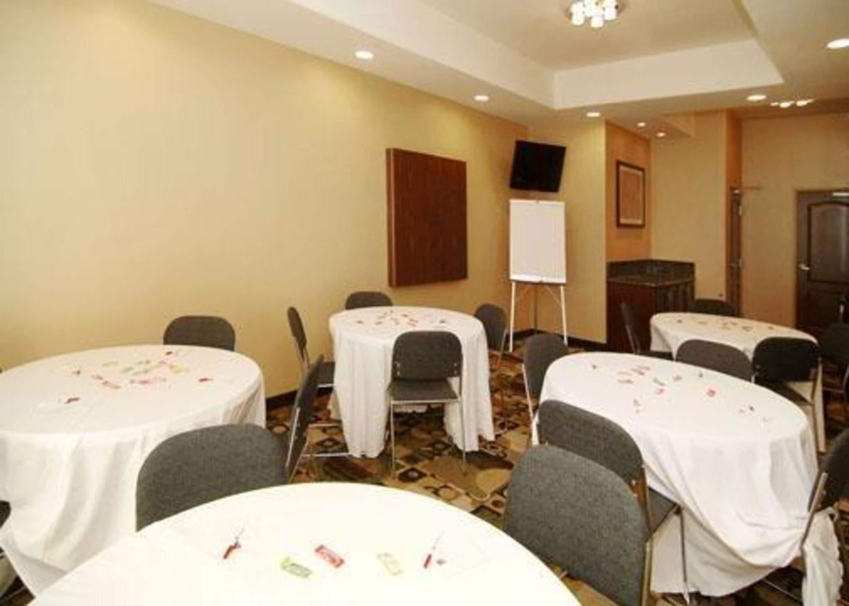 A conference room with round tables, chairs, a whiteboard, and a television on the wall.