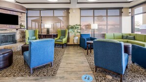 A modern lounge area with a fireplace, comfortable seating, large windows, and a patterned floor.