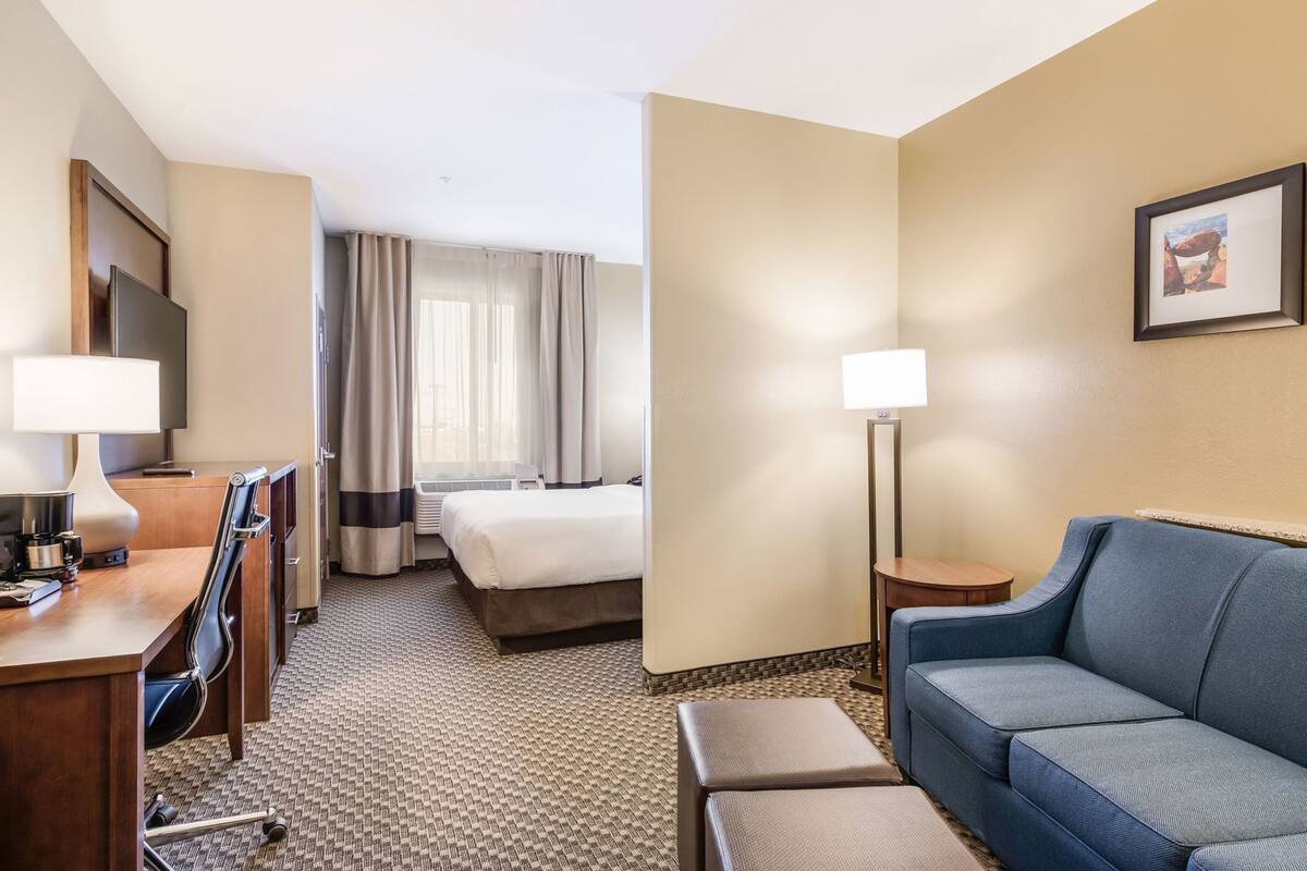 Ein Hotelzimmer mit einem Bett, einem Schreibtisch mit Lampe, einem Sessel und einem Sofa sowie einer Stehlampe.