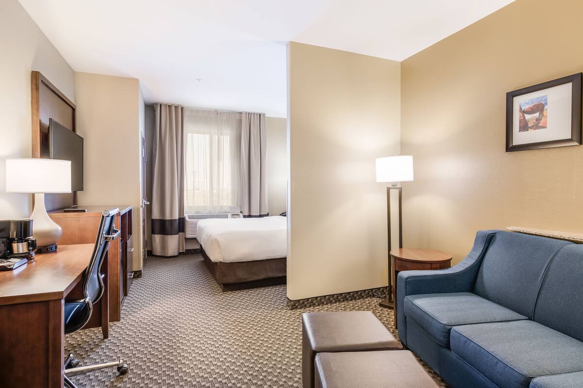 Ein Hotelzimmer mit einem Bett, einem Schreibtisch mit Stuhl, einer Couch, einem Fernseher und einer Lampe.