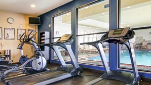 A gym with three treadmills, a pool visible through large windows, and exercise equipment.