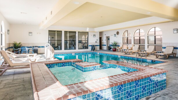 A swimming pool with tiled edges, lounge chairs, and a sunshade.