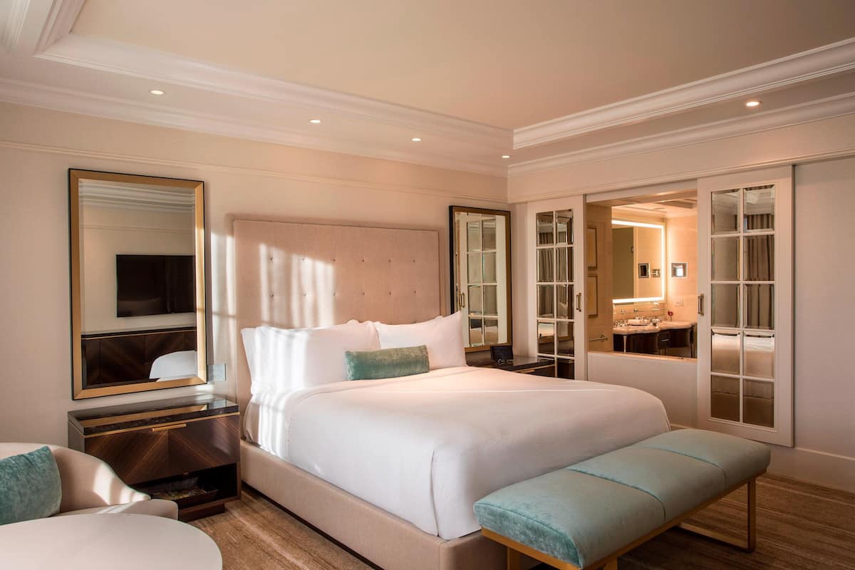 A spacious bedroom with a large bed, bedside tables, a bench, and a mirror.