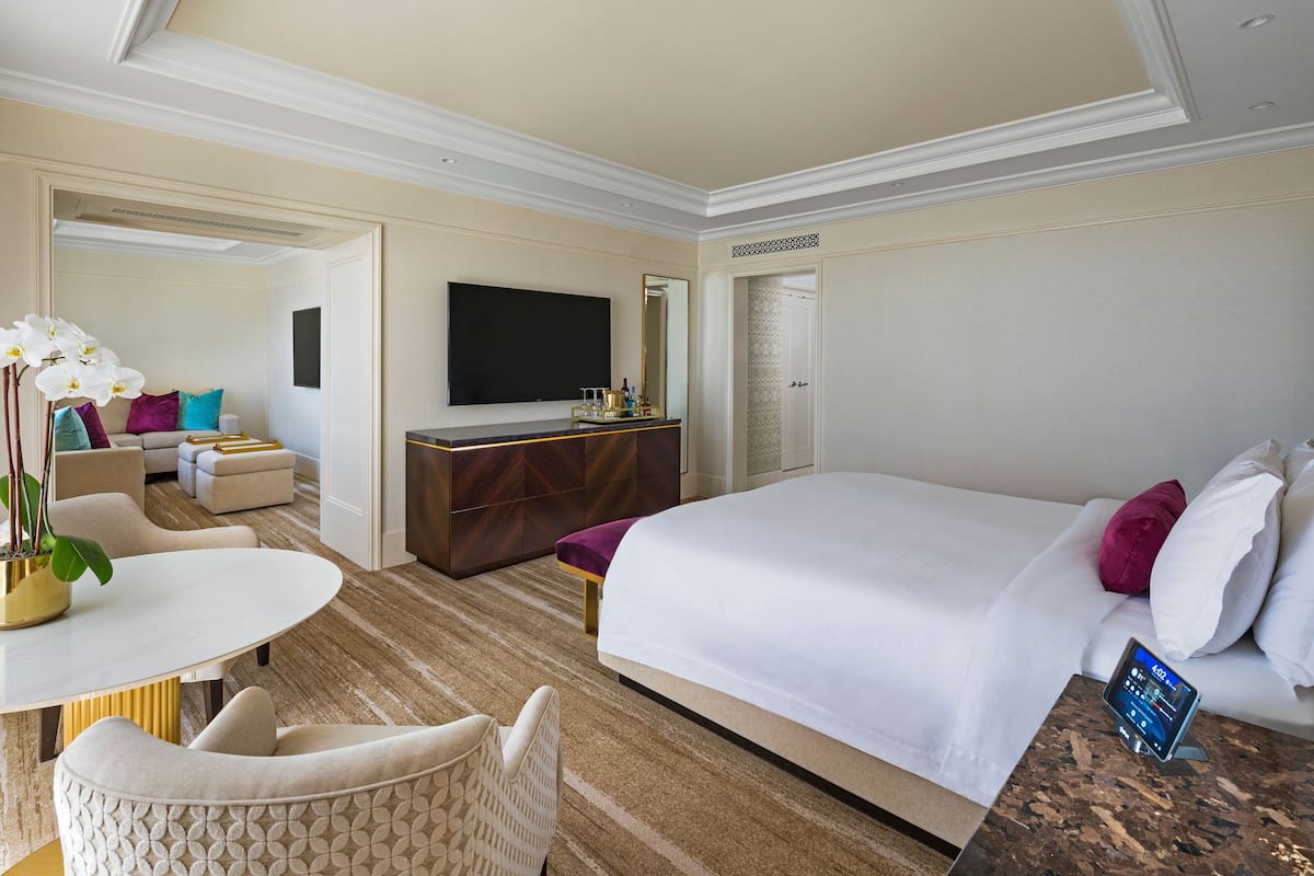 A hotel room with a large bed, a TV, a desk with a chair, and a sofa.