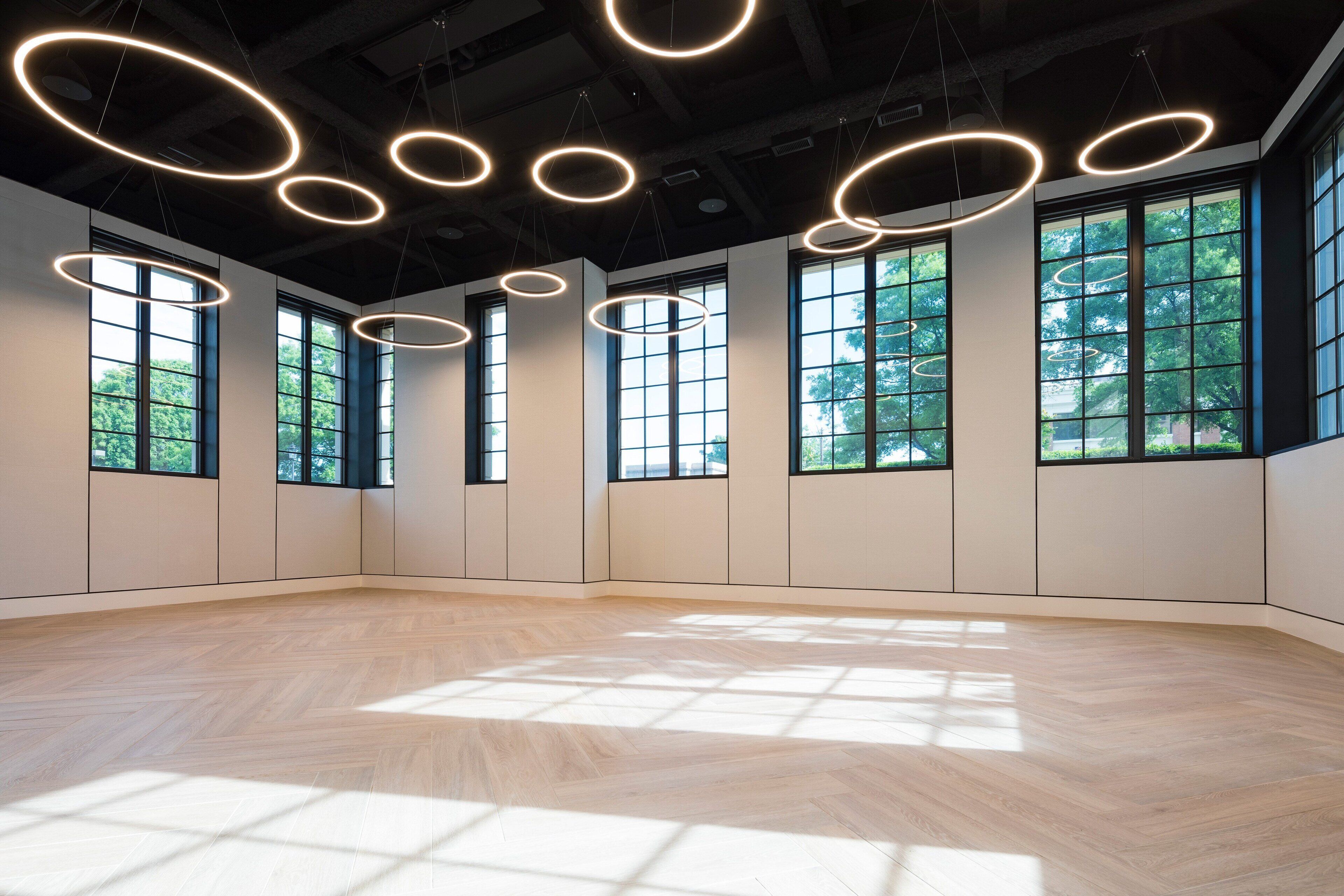 A spacious room with large windows, wooden flooring, and modern circular light fixtures.