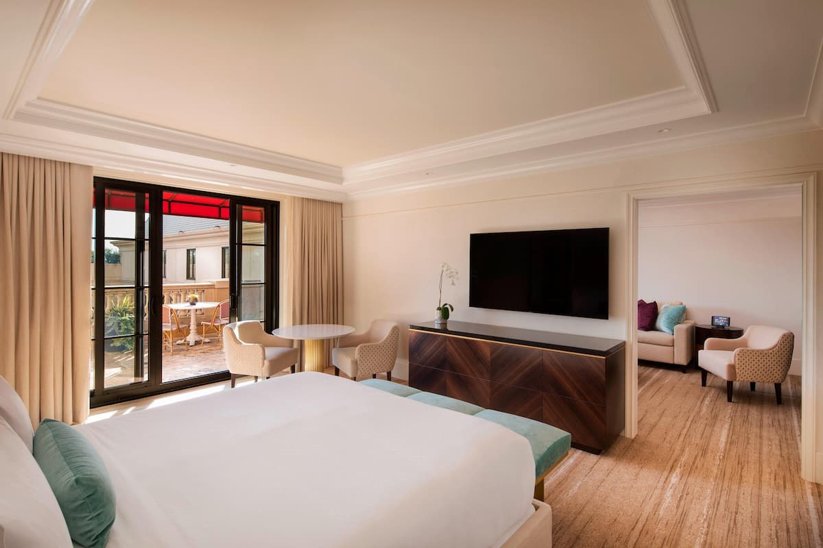 A hotel room with a large bed, a TV, a desk, and a seating area with a view to the outside.