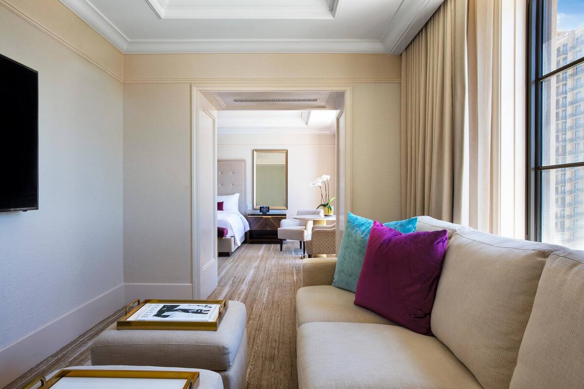 A hotel room with a sofa, ottoman, and a flat-screen TV mounted on the wall.