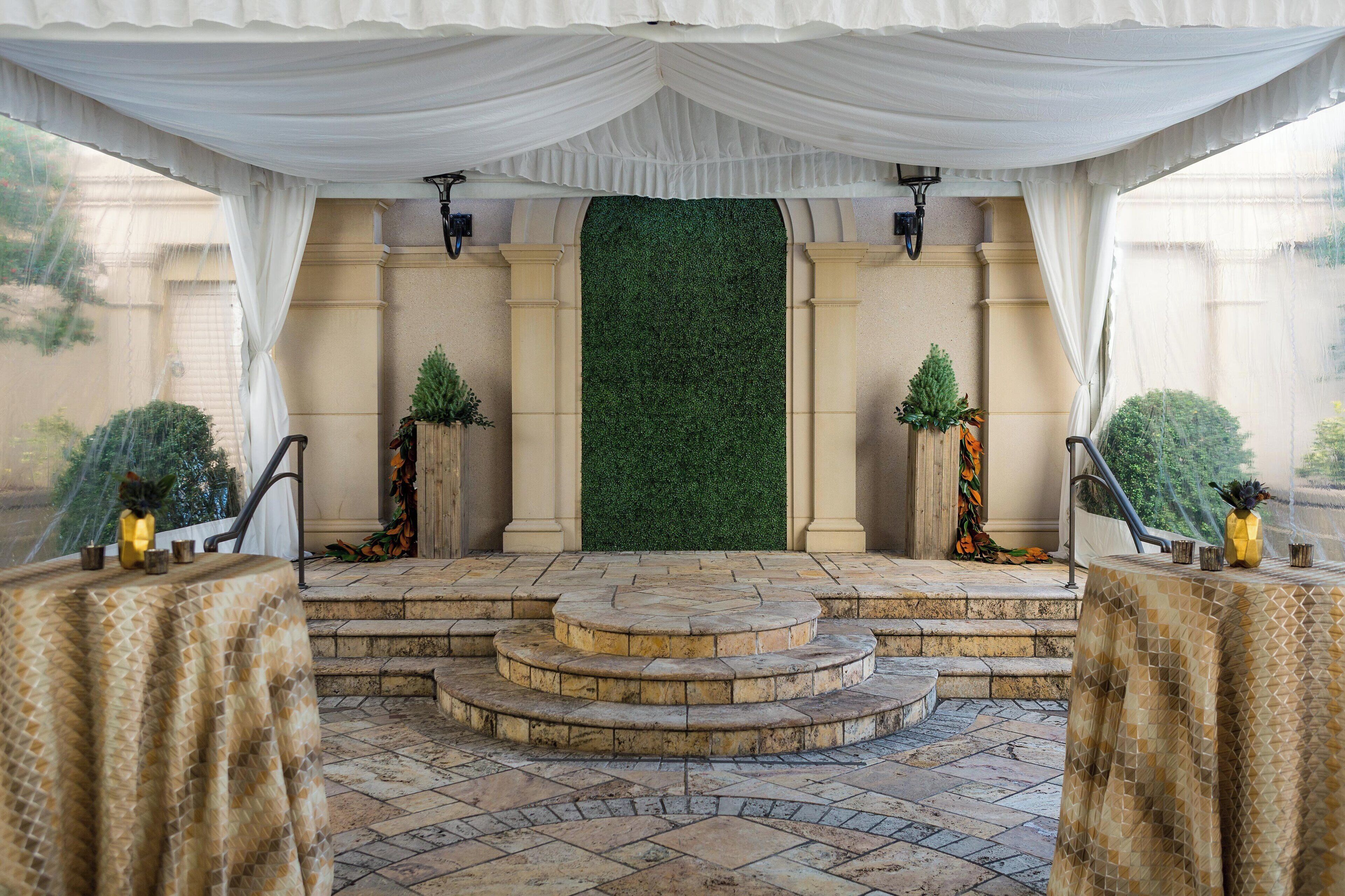 Ambiente formal ao ar livre, com fundo verde, degraus de pedra e mesas com toalhas estampadas.