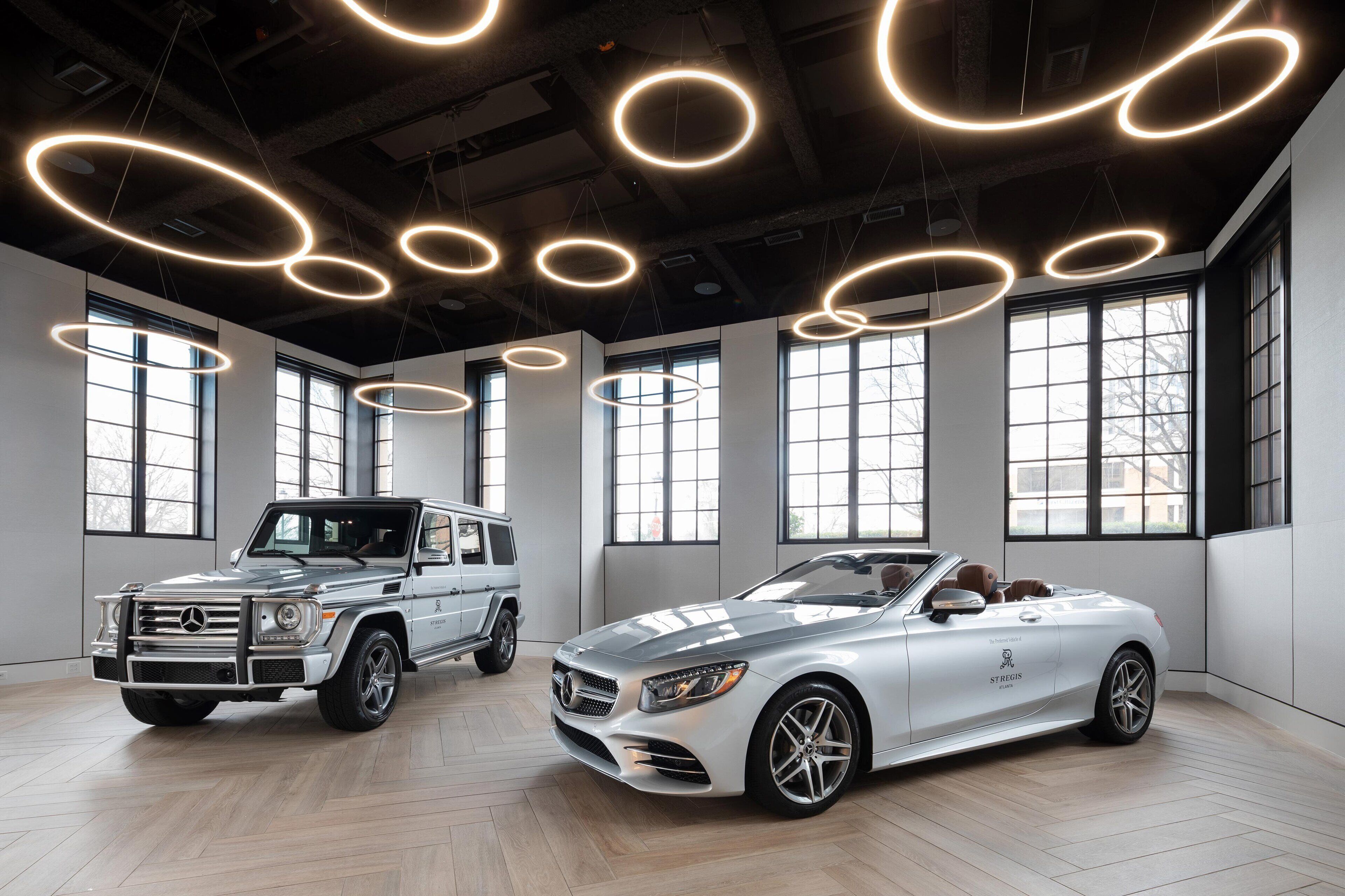 A showroom with two luxury cars, a convertible and a SUV, in a spacious interior with large windows and modern lighting.