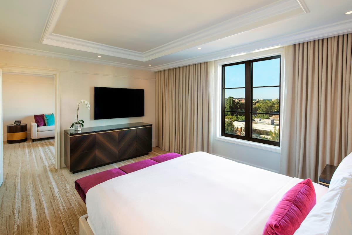 A hotel room with a large bed, a flat-screen TV, a view of the city, and a balcony.