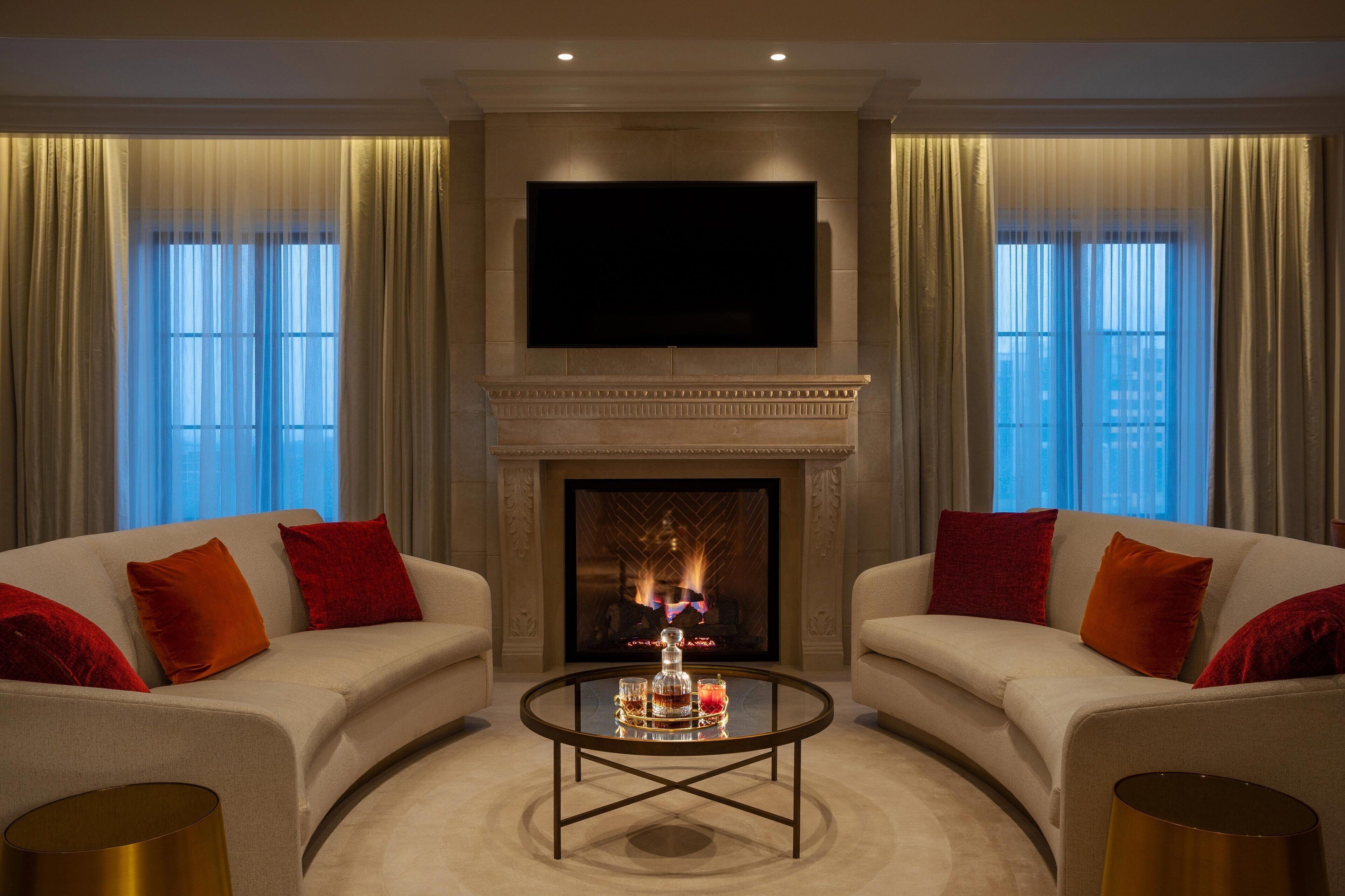 A living room with a fireplace, two sofas, a coffee table, and a flat-screen TV mounted above the fireplace.