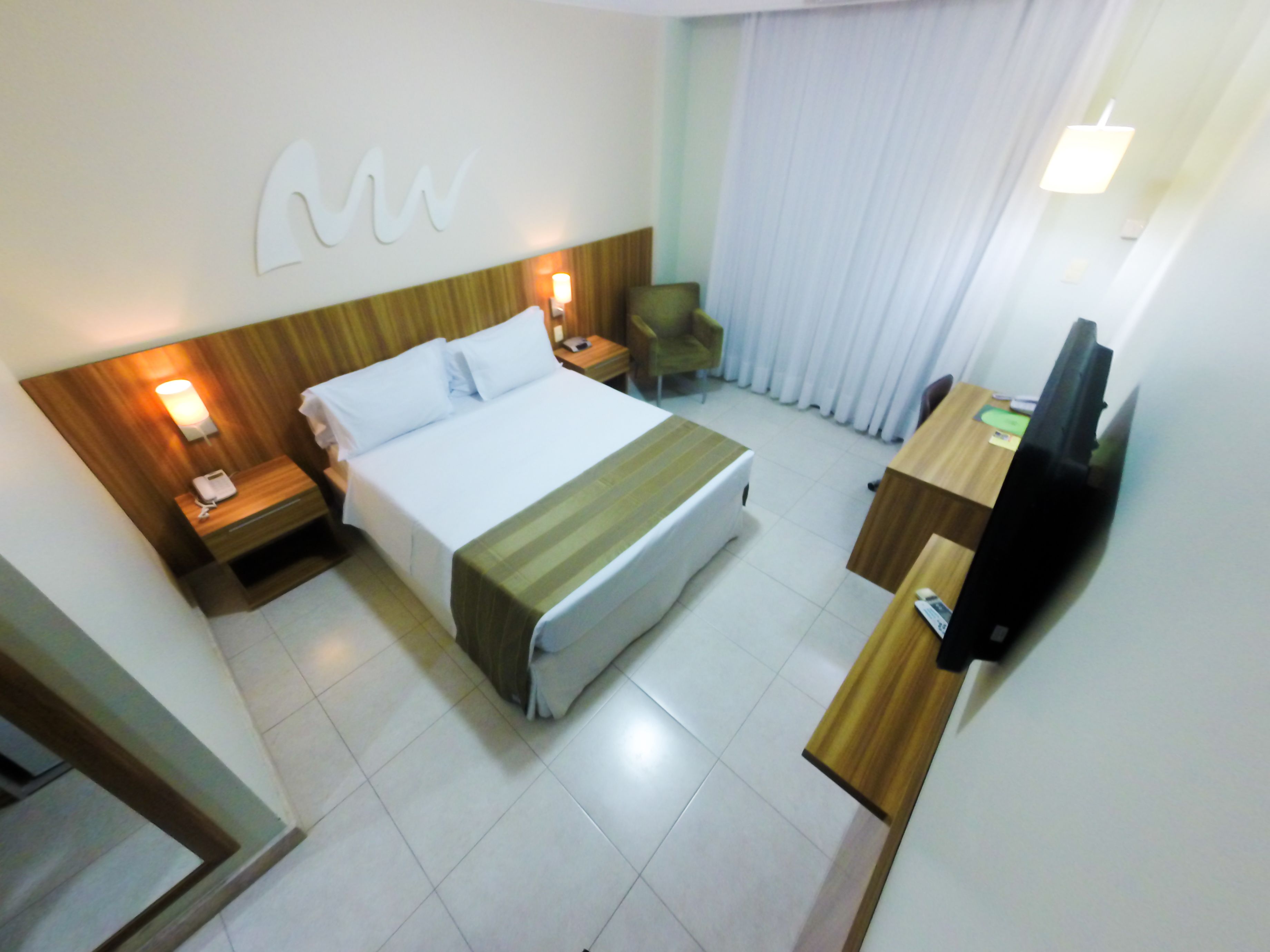 A hotel room with a bed, bedside tables, a desk, a chair, and a television.