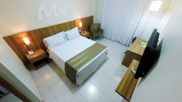 A hotel room with a bed, bedside tables, a desk, a chair, and a television.