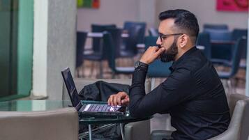 Uma pessoa sentada a uma mesa com um laptop, num espaço com cadeiras e um painel de vidro.