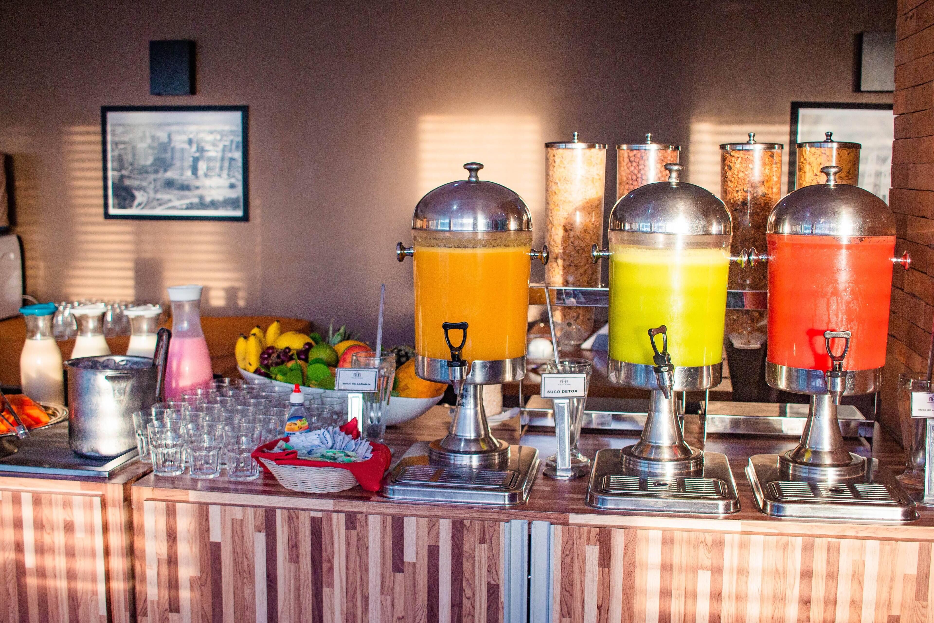 Een ontbijtbuffet met sapautomaten, een schaal fruit en een koffiehoek.