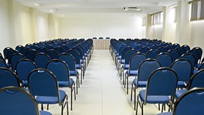 A conference room with rows of blue chairs and a white table at the front. - Real Classic Hotel (Aracaju)