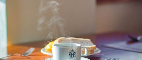 Uma chávena de café com vapor a subir, uma fatia de torrada e um pequeno recipiente de manteiga sobre uma mesa de madeira.