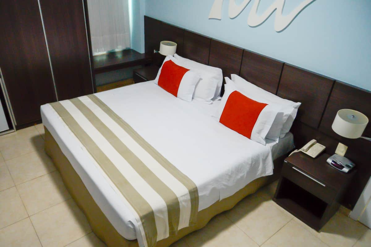 A hotel room with a large bed, a nightstand with a lamp, and a wall with a large letter 'W'.