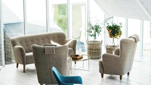Un salon moderne avec un plafond haut et de grandes fenêtres, comprenant un canapé beige, un fauteuil bleu et une petite table basse.