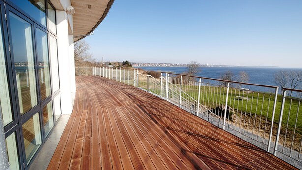 Une terrasse en bois offrant une vue sur la mer et sur les bâtiments d’une ville située au loin.