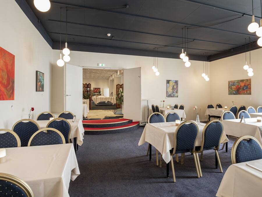 Uma sala de conferência com mesas redondas, cadeiras e um palco.