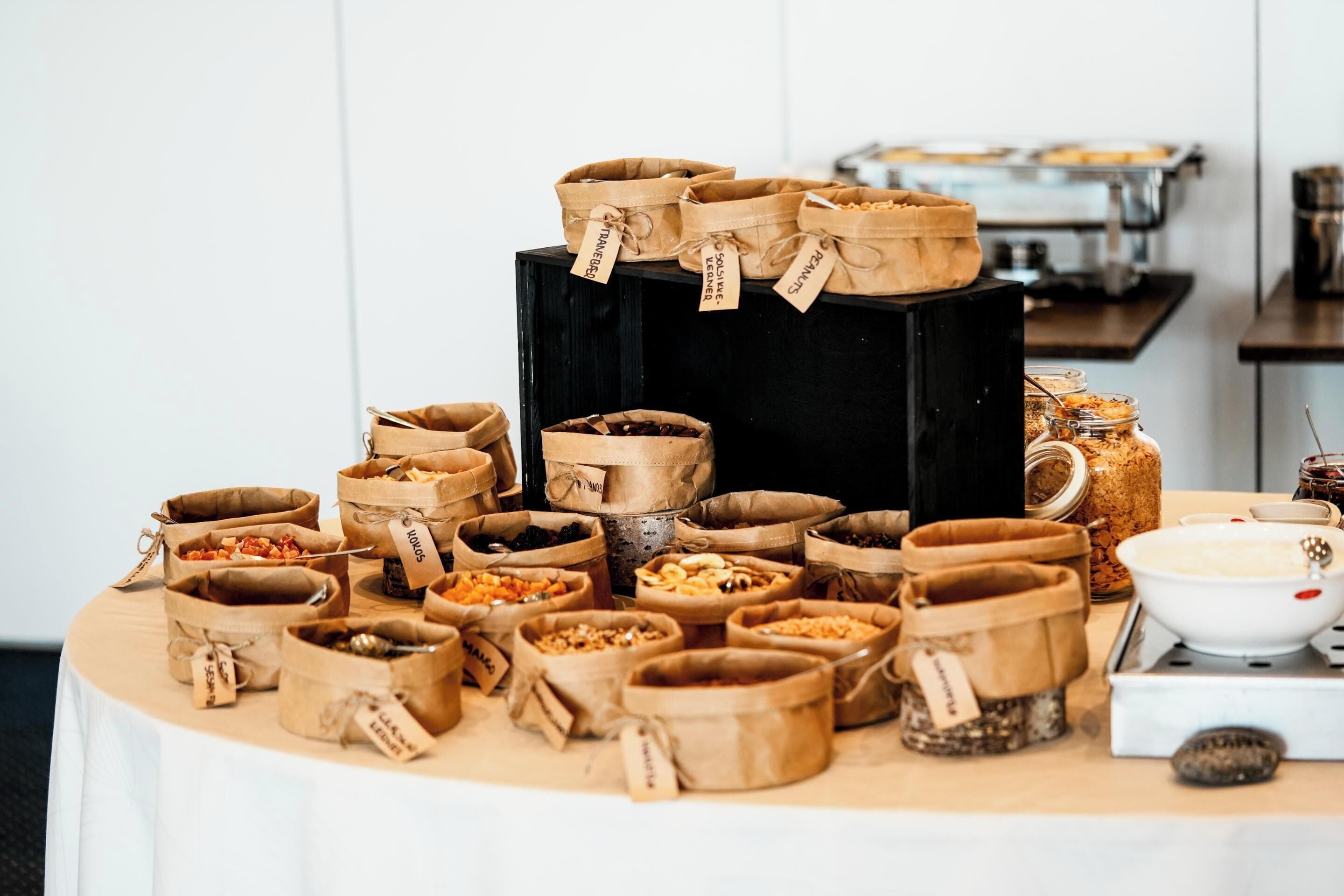 Una mesa de buffet con diversos alimentos en bolsas de papel, una máquina de café y un frasco de salsas.