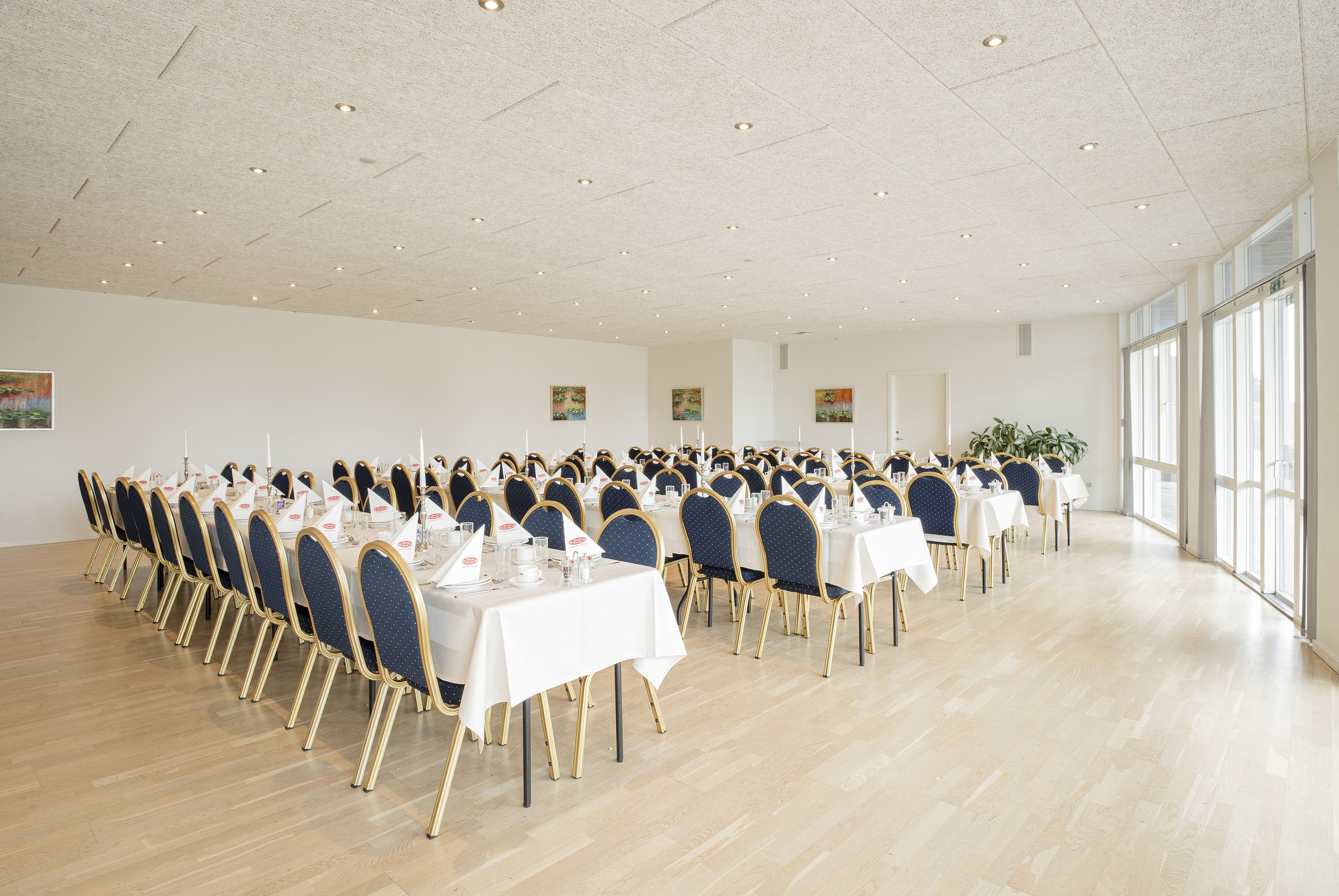 A large, well-lit conference room with rows of tables and chairs, large windows, and artwork on the walls.