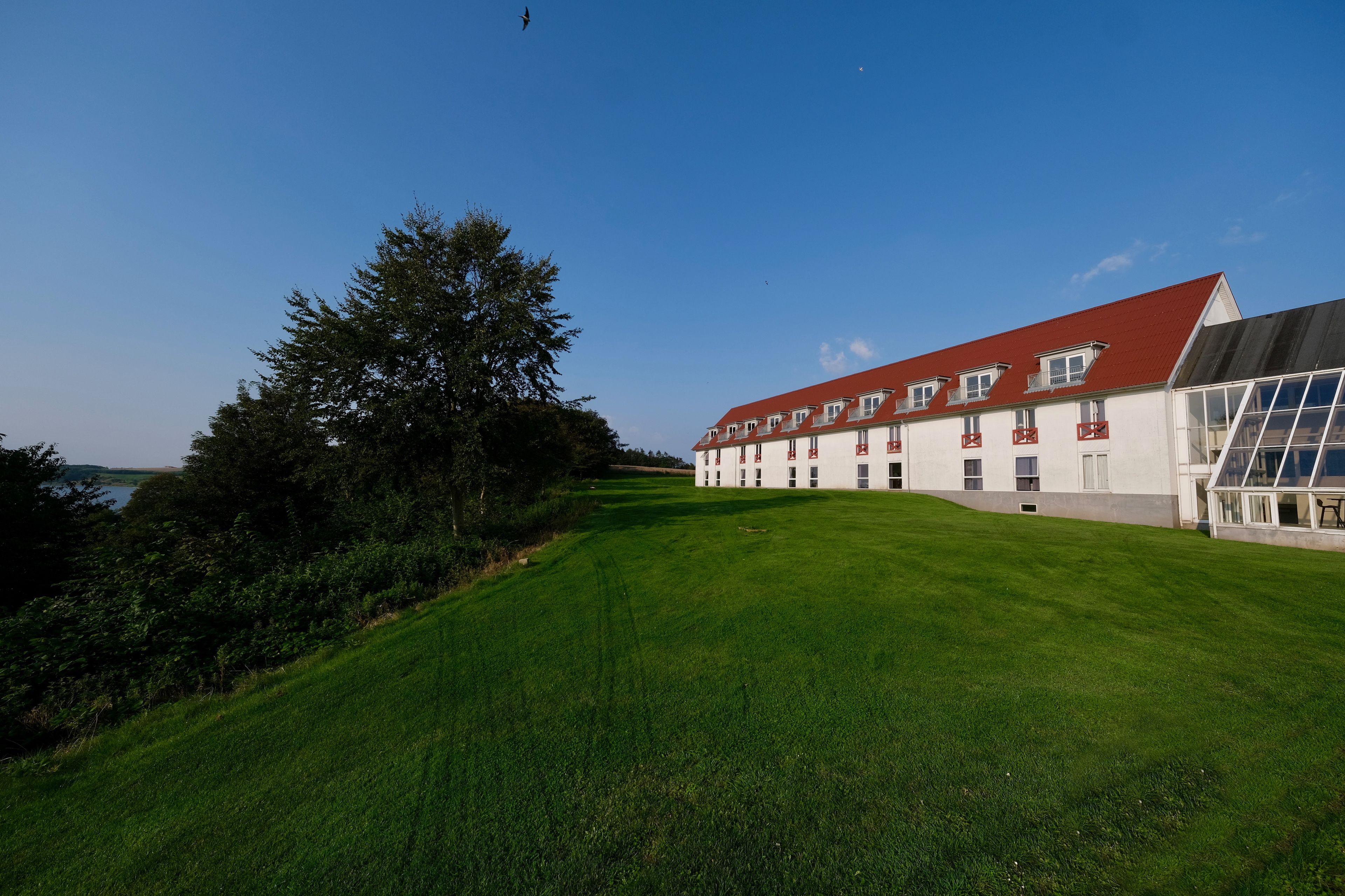 A large building with a red roof and white walls, surrounded by a well-maintained lawn and trees.