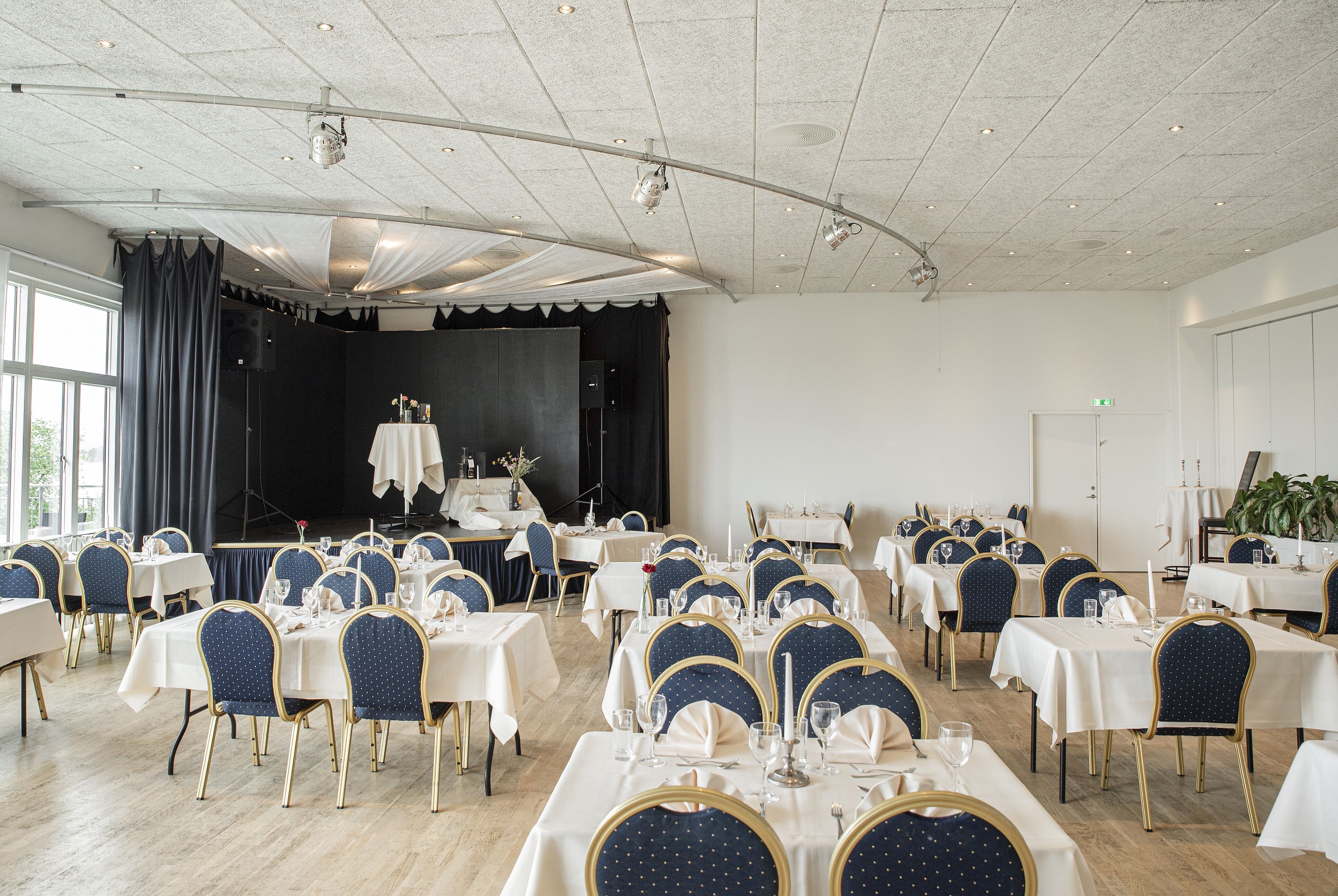 A banquet hall with multiple round tables, each set with white tablecloths and blue chairs.