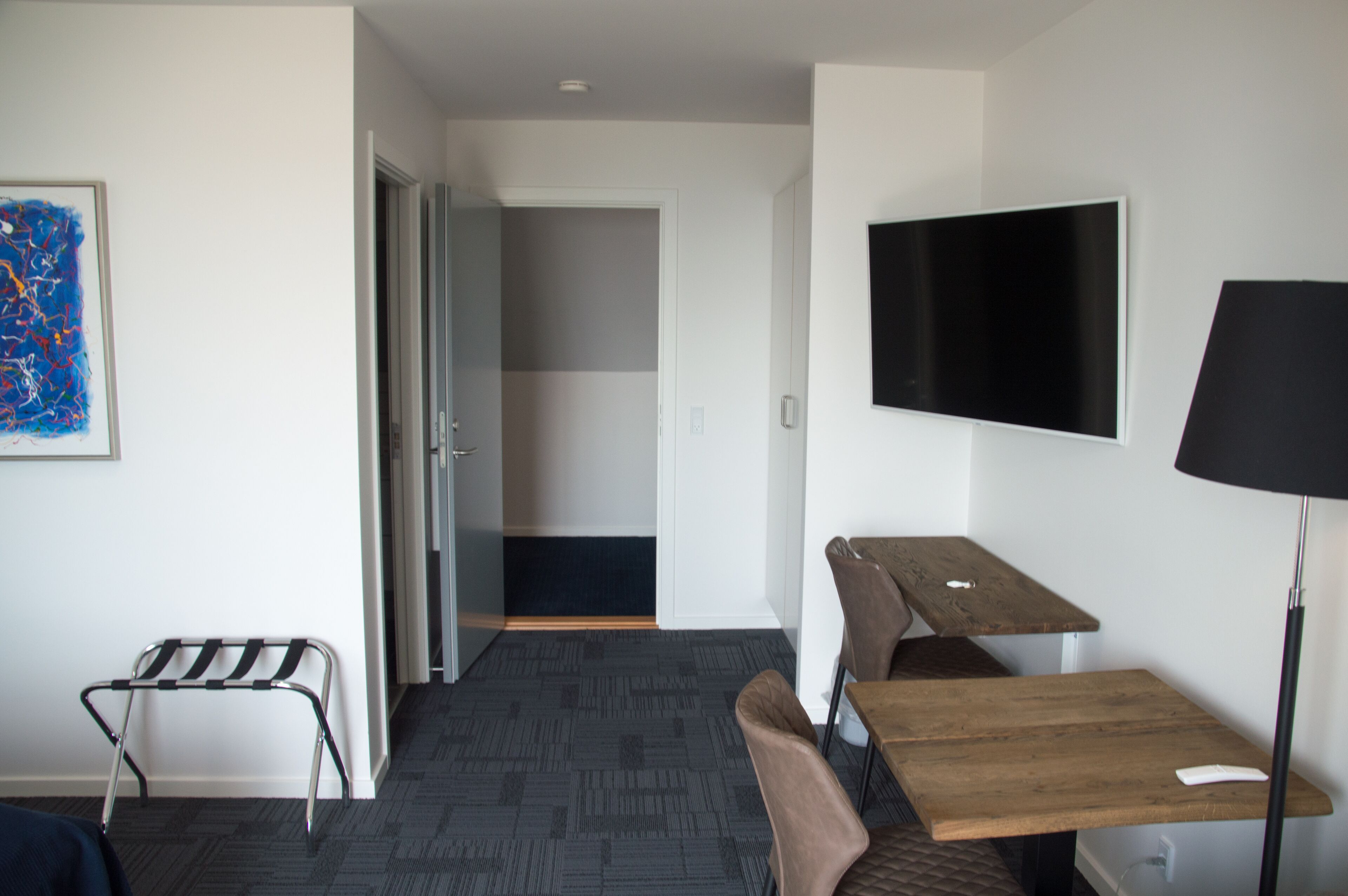 A hotel room with a bed, a desk, a chair, a TV, and a door leading to another room.
