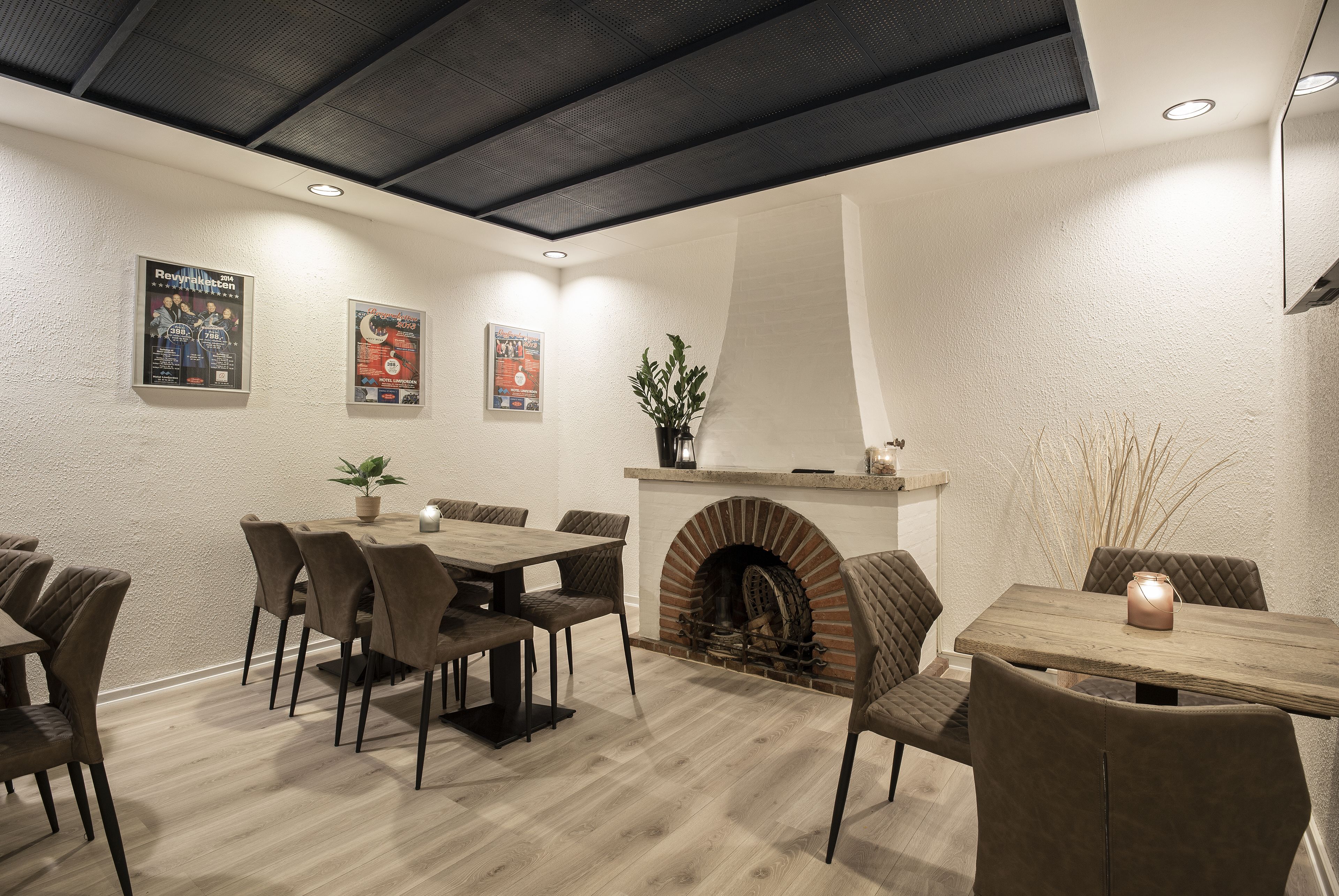 A dining area with a brick fireplace, wooden flooring, and a ceiling with a black panel.