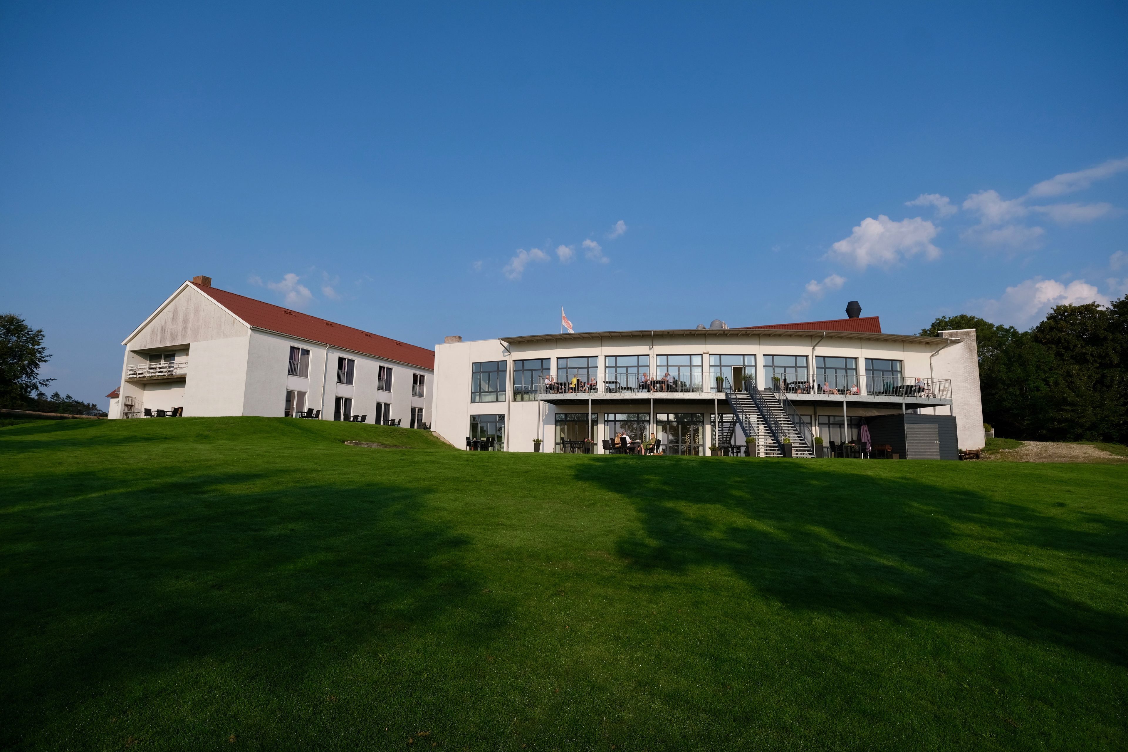 A modern building with a red roof, large windows, and a grassy lawn.