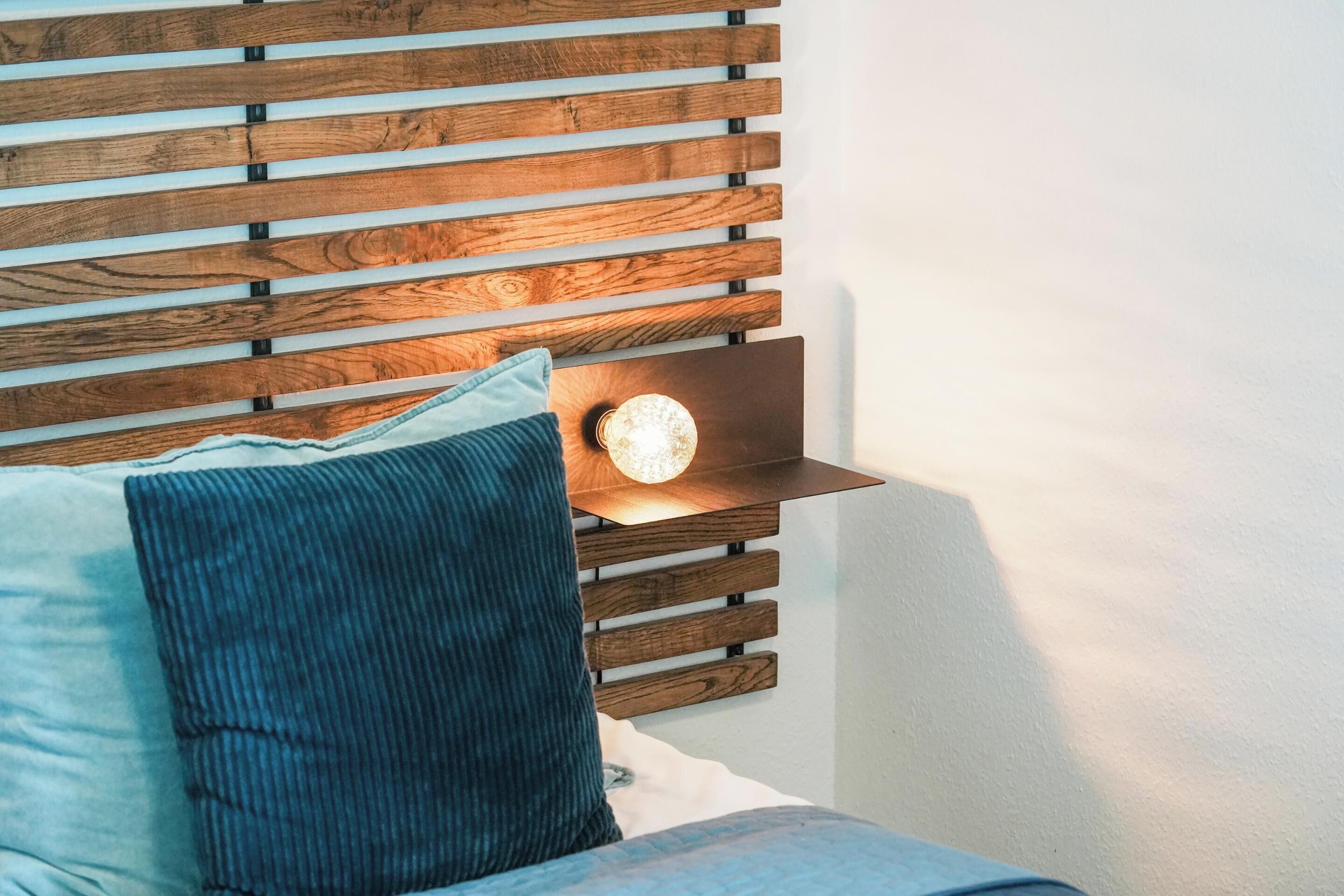 A bed with a wooden headboard, a bedside lamp, and a pillow.