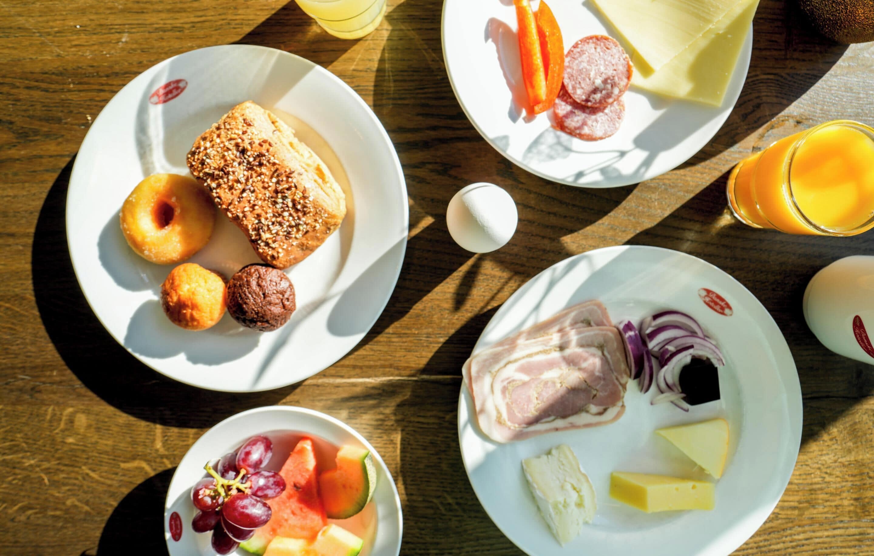 A table with plates of food including bread, sausages, cheese, and fruits.