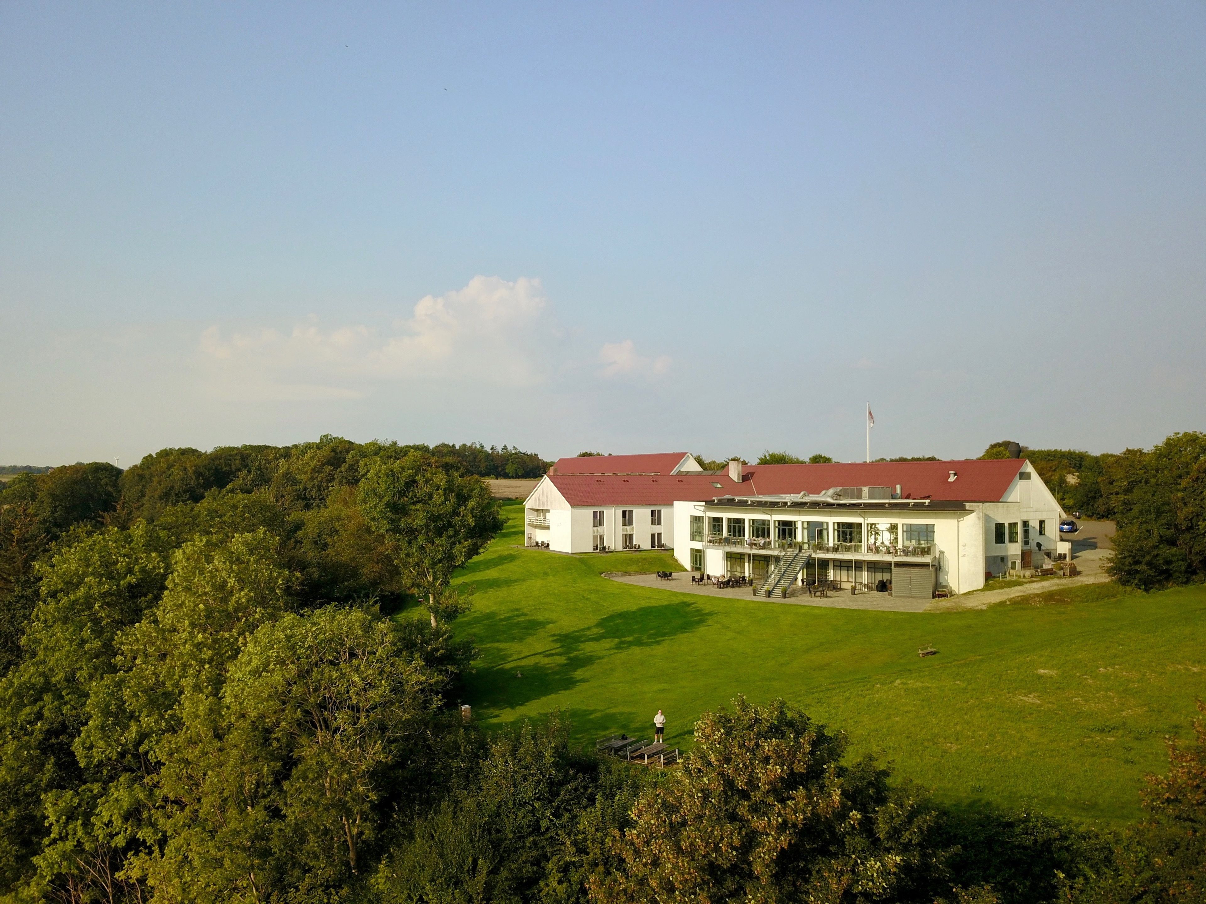 A large, white building with a red roof, surrounded by lush greenery and a well-maintained lawn.