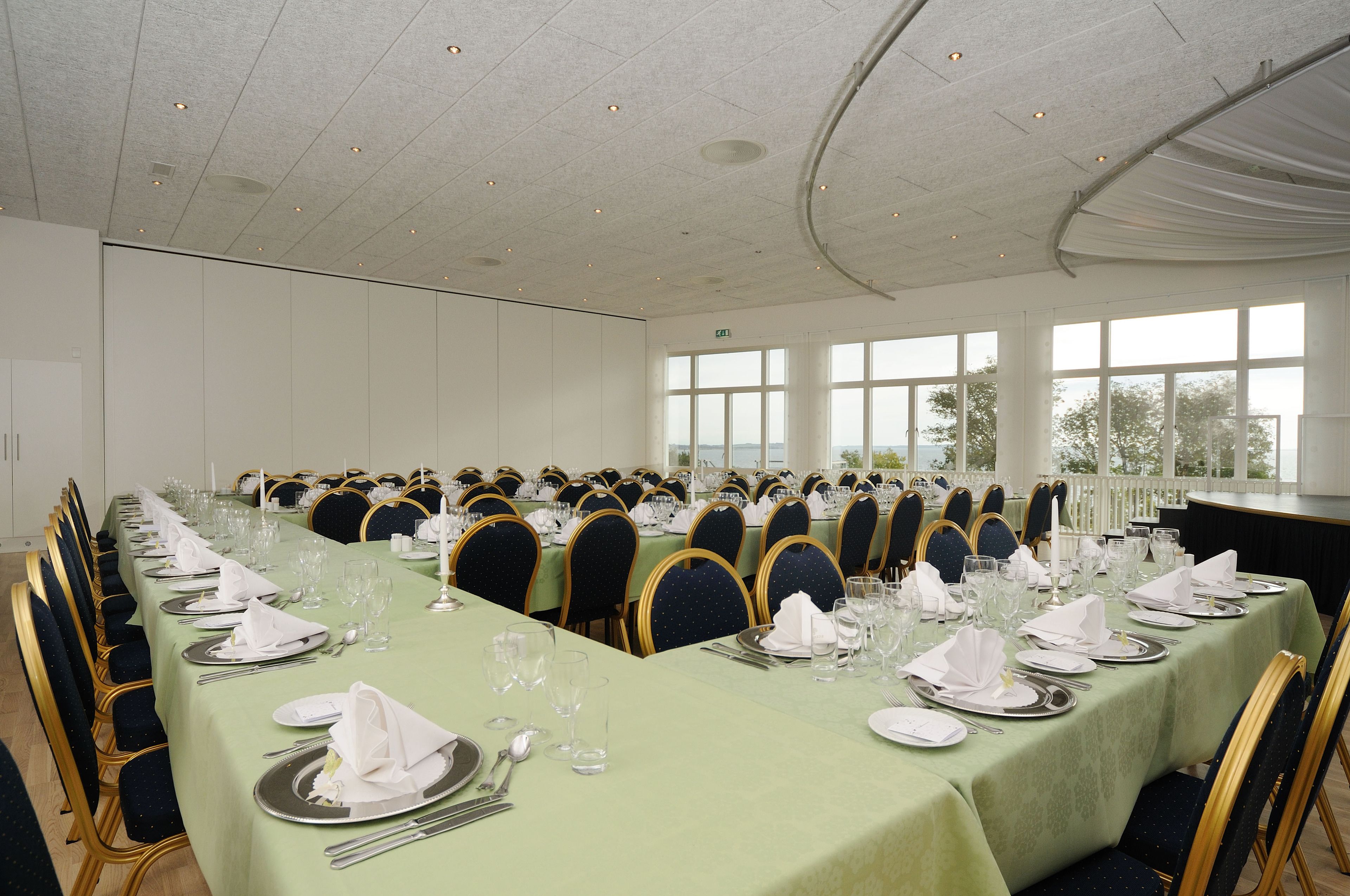Un salón de banquetes con largas mesas dispuestas para un evento formal, con sillas con detalles dorados y un mantel verde.