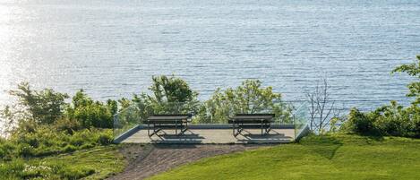 A lakeside deck with two wooden benches and a glass railing overlooking the water.