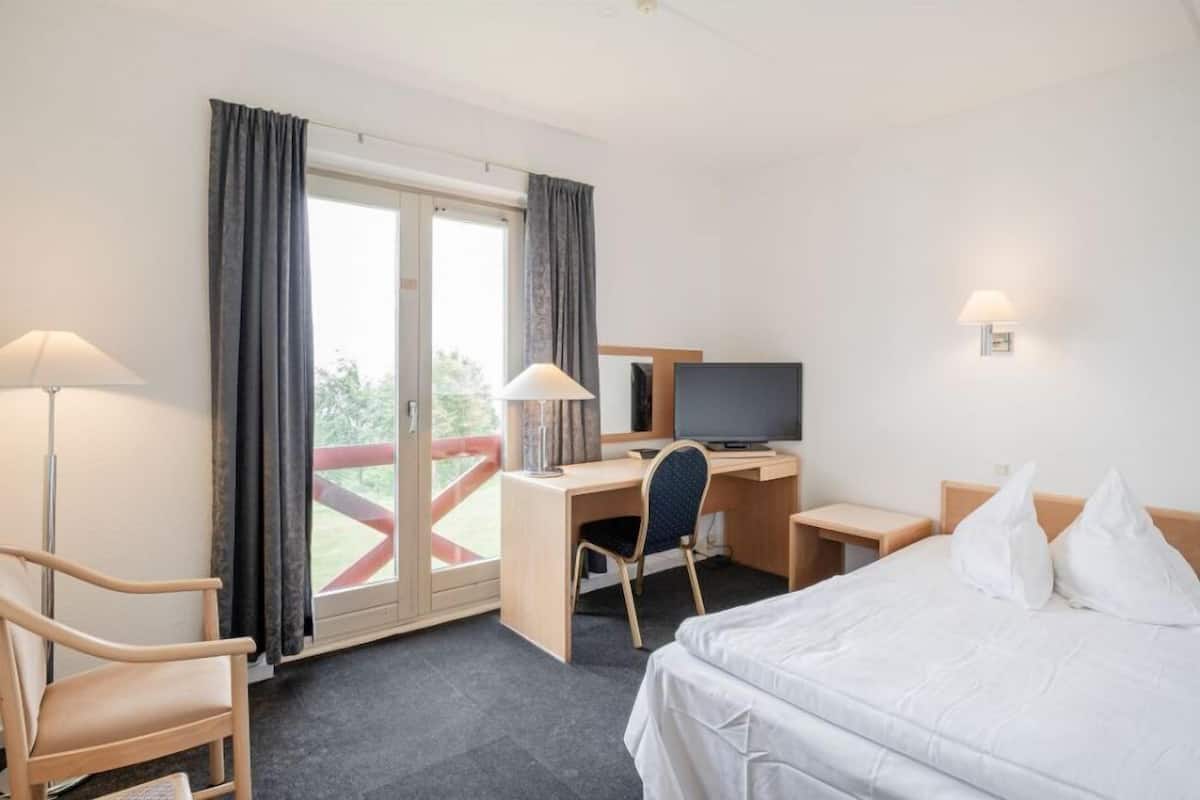 A hotel room with a bed, desk, chair, television, and a window with curtains.