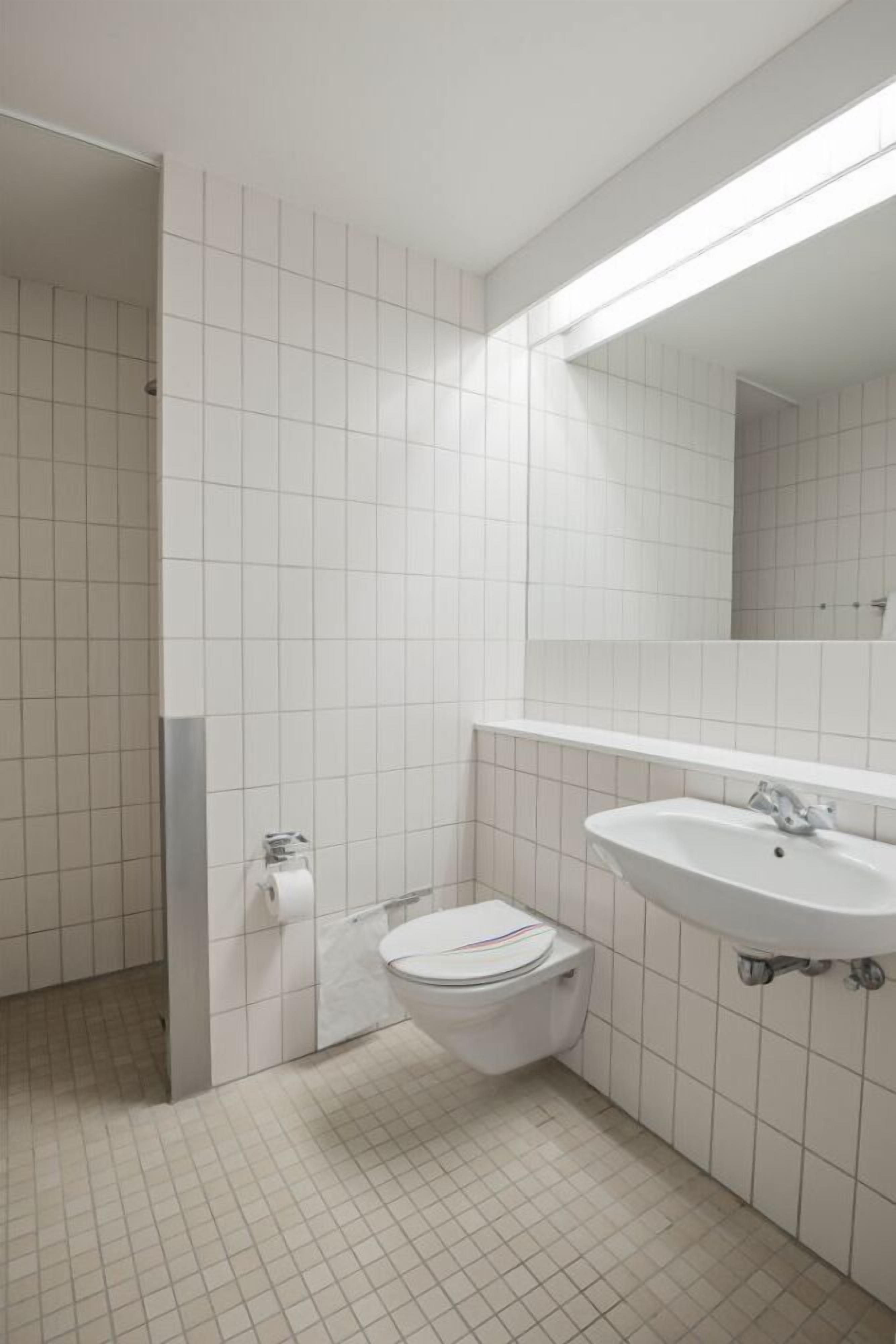 Un baño pequeño y limpio con azulejos blancos, un inodoro, un lavabo y un espejo.