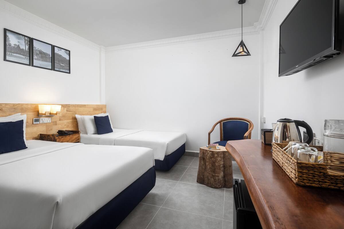 Une chambre d’hôtel avec deux lits, une tête de lit en bois, une télévision, une table basse et une chaise.