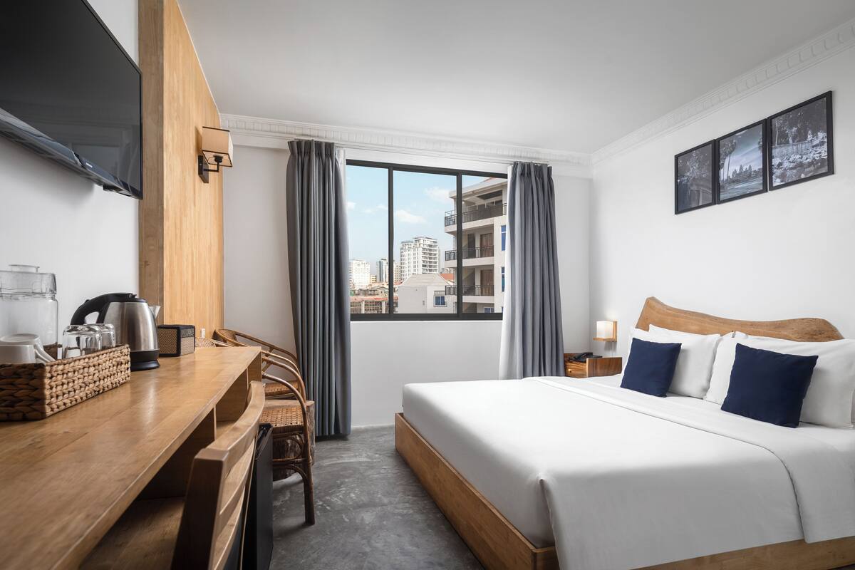 Une chambre d’hôtel équipée d’un lit, d’un bureau, d’une chaise, d’une télévision et d’une fenêtre avec des rideaux.