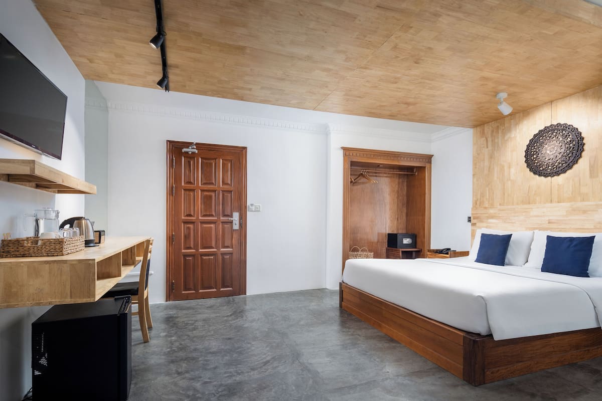 Une chambre moderne avec un plafond en bois, un lit avec des oreillers bleus, un bureau avec un ordinateur et un téléviseur fixé au mur.